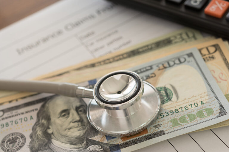 A stack of dollar bills and claim form with a stethoscope on top. | Corporate Synergies