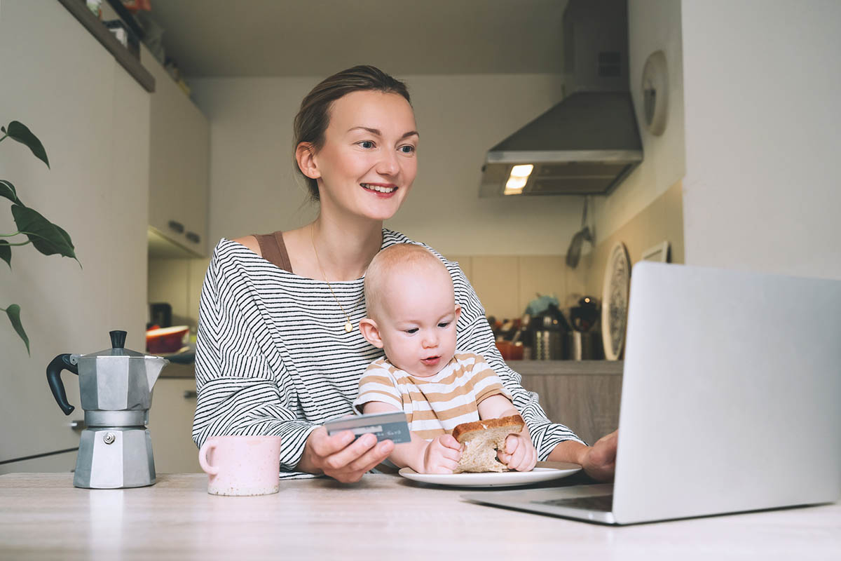 a young woman on paid family leave with her baby sits at a laptop /Corporate Synergies