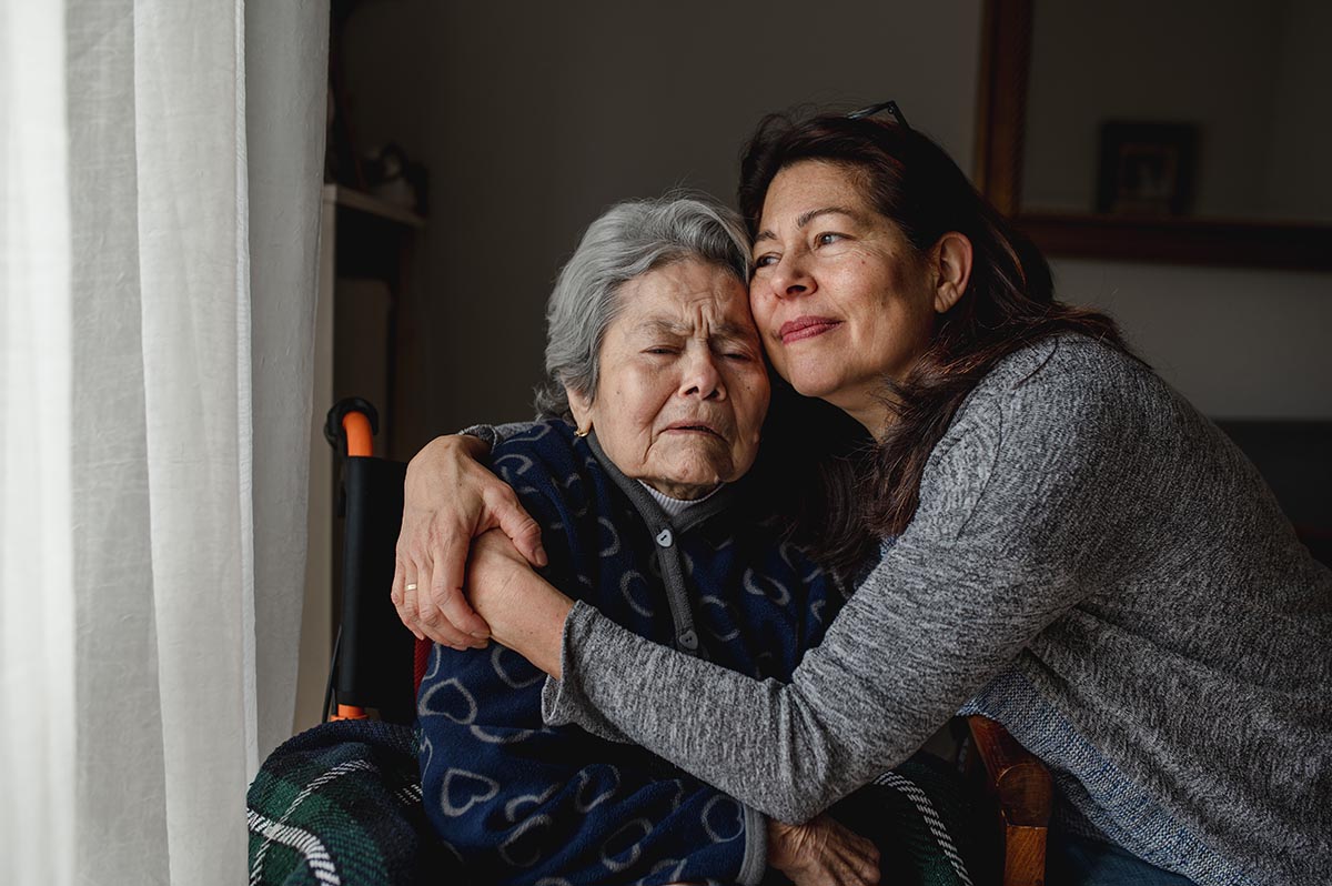 caregiver employee hugs her ill mother while they sit together |Corporate Synergies