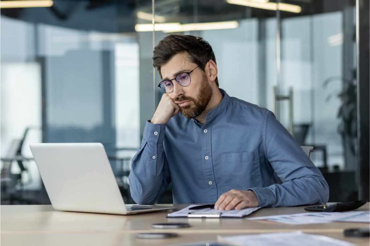 A disengaged manager sits at his laptop, head on his closed fist looking exhausted | Corporate Synergies