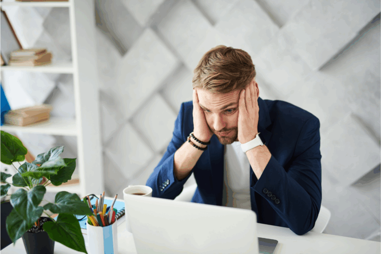 A frustrated man stares at the computer reviewing his benefits during a life crisis| Corporate Synergies