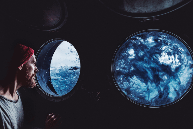A man stares out a porthole at rough waters while steadying the ship | Corporate Synergies