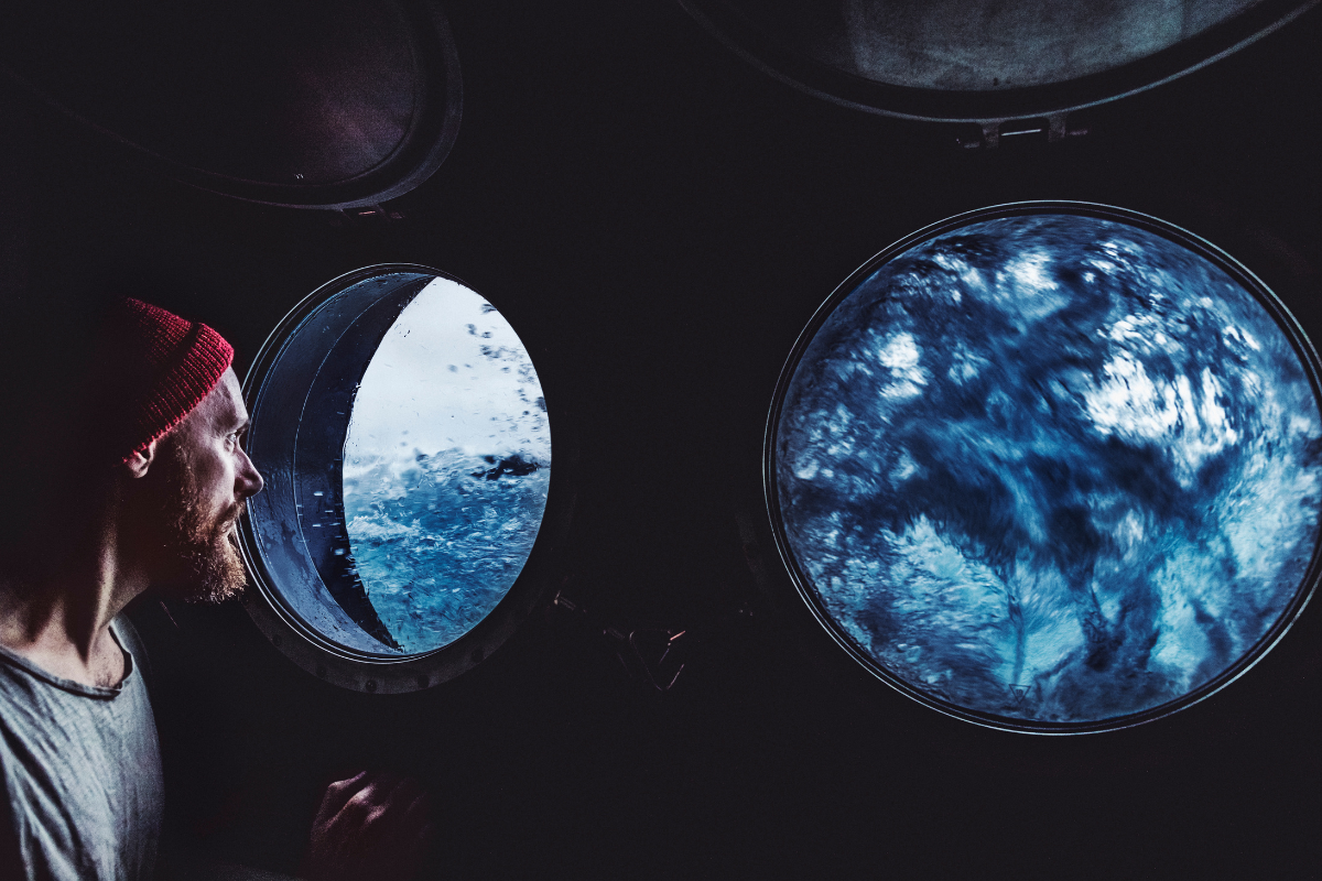 A man stares out a porthole at rough waters while steadying the ship | Corporate Synergies