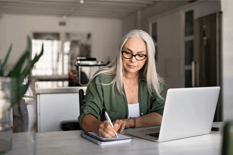 Older employee takes notes at her laptop illustrating the missing link of benefits literacy| Corporate Synergies