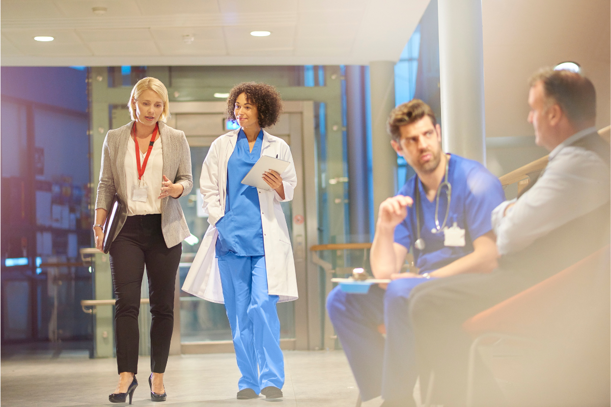 HR admin discusses recent healthcare shifts with a doctor in hospital corridor| Corporate Synergies