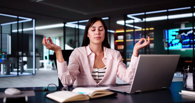 Woman meditates at office desk enjoying her mental health and well-being benefits| Corporate Synergies