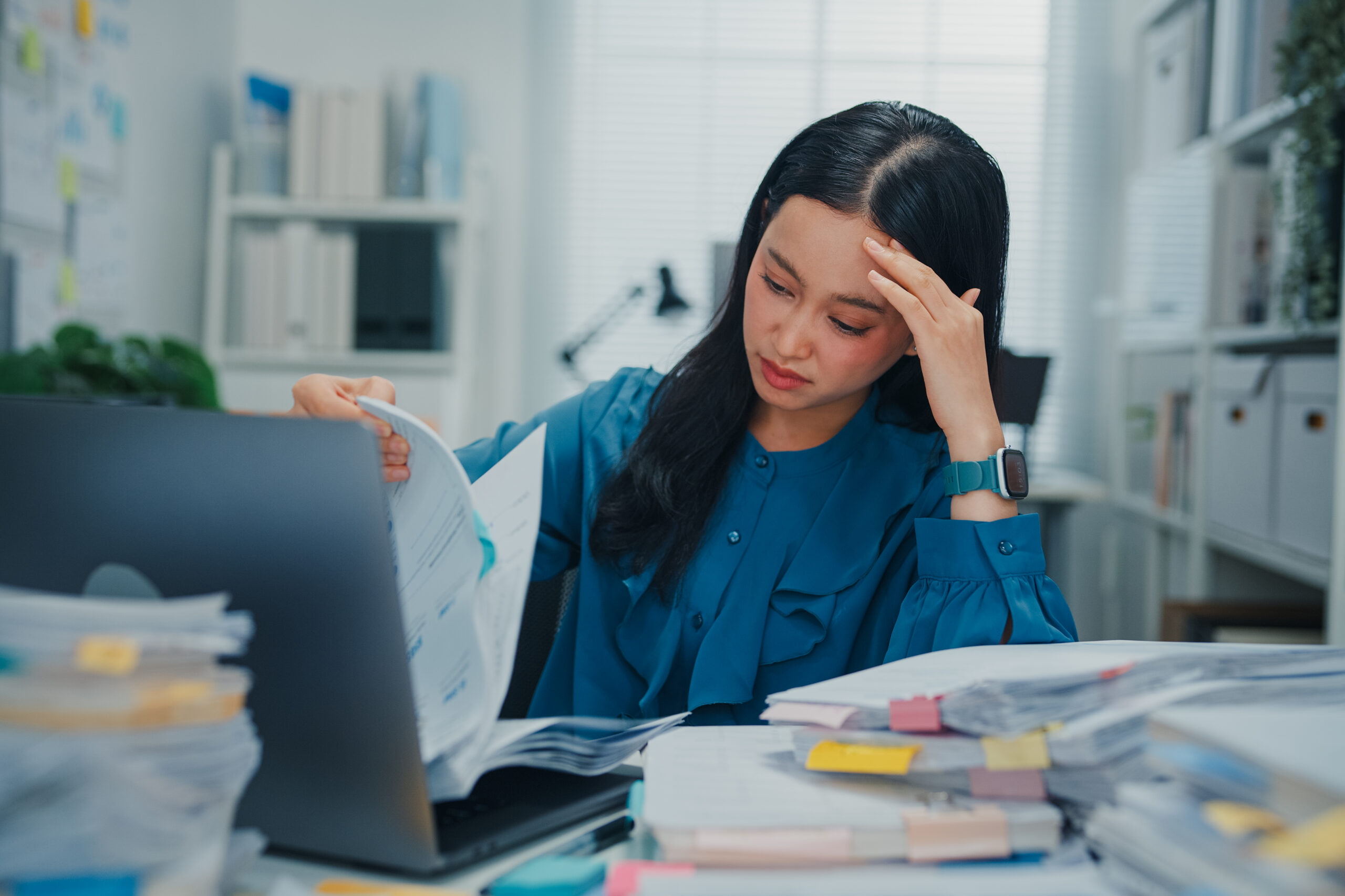 HR professional feeling administrative strain holds her head while reviewing employee benefits concerns. |Corporate Synergies